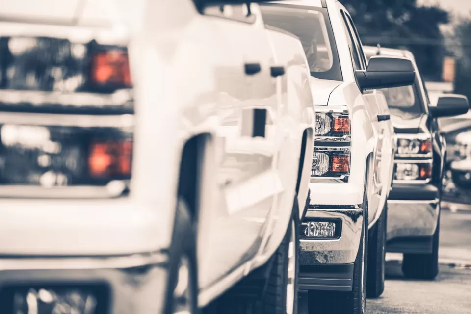 Close-up of white pick-up truck on sales lot from front driver's side; two more trucks behind it
